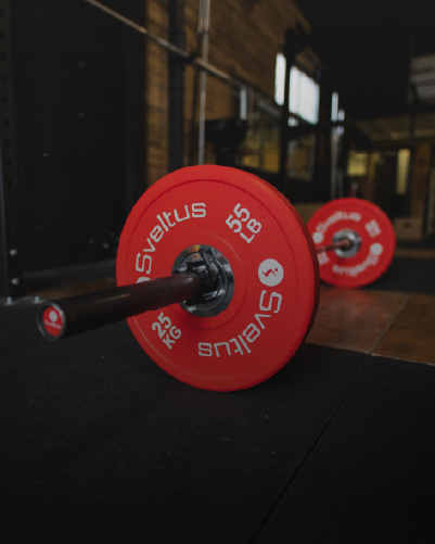 une barre et des disques olympique compétition de 25kg et de couleur rouge posés au sol sur des dalles
